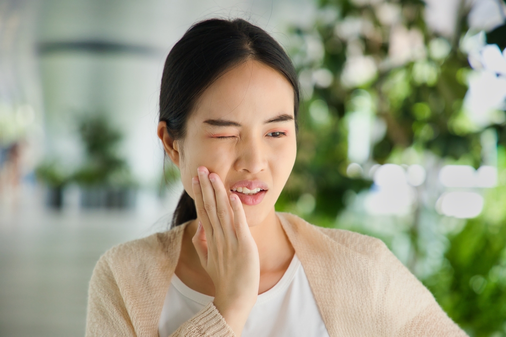 Young woman holding cheek in discomfort, representing urgent care and relief through Dental Services at West Kerr Dental