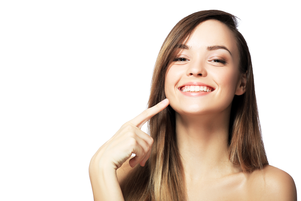 Smiling woman pointing at teeth, showcasing confidence with Invisalign treatment available at West Kerr Dental