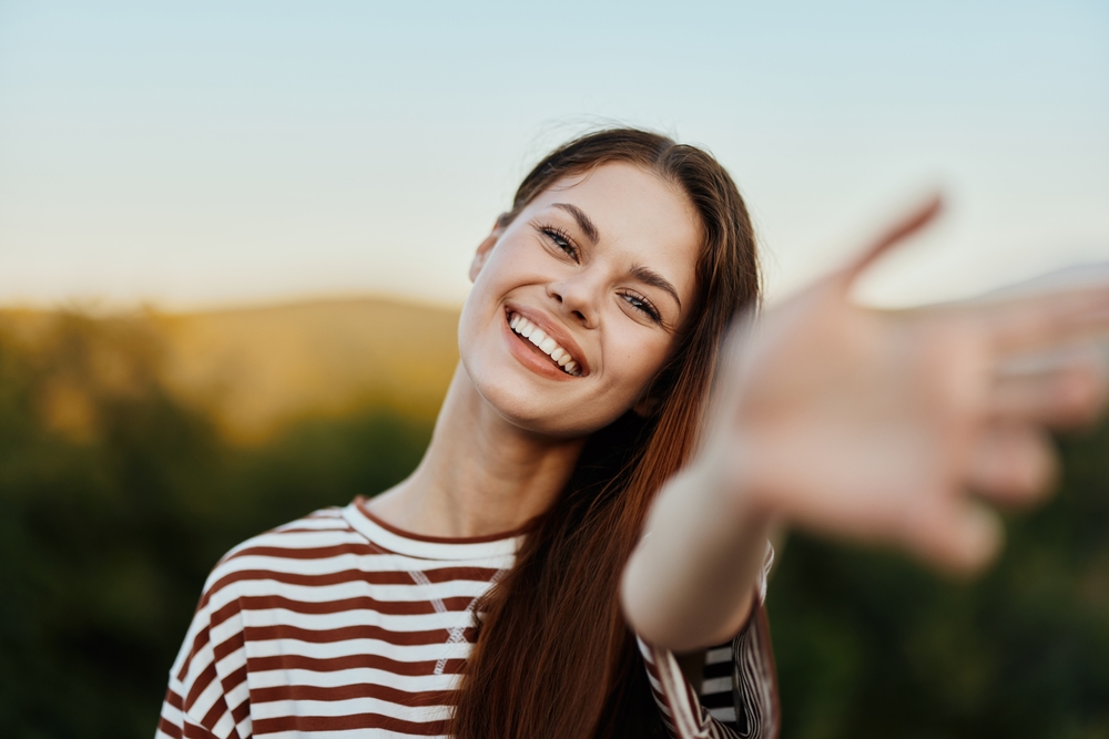 Smiling young woman outdoors reaching playfully, showcasing bright healthy teeth with Dental Services at West Kerr Dental